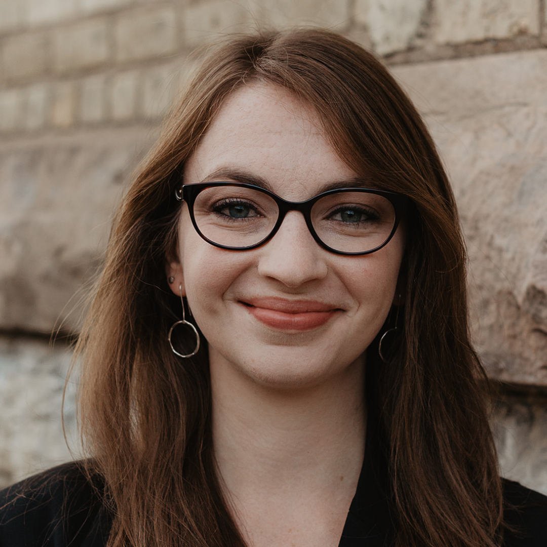 A smiling woman stands in front of a brick wall